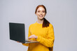 © dikushin - Cheerful young business woman or student holding laptop computer and looking at camera on isolated gray background. Pretty redhead lady model emotionally showing facial expressions, copy space.