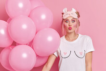 Photo Of Good Looking European Woman Wears Bright Makeup Wears Sleepmask And White Casual T Shirt Has Romantic Mood During Dance Party Holds Bunch Of Balloons Isolated Over Pink Studio Background