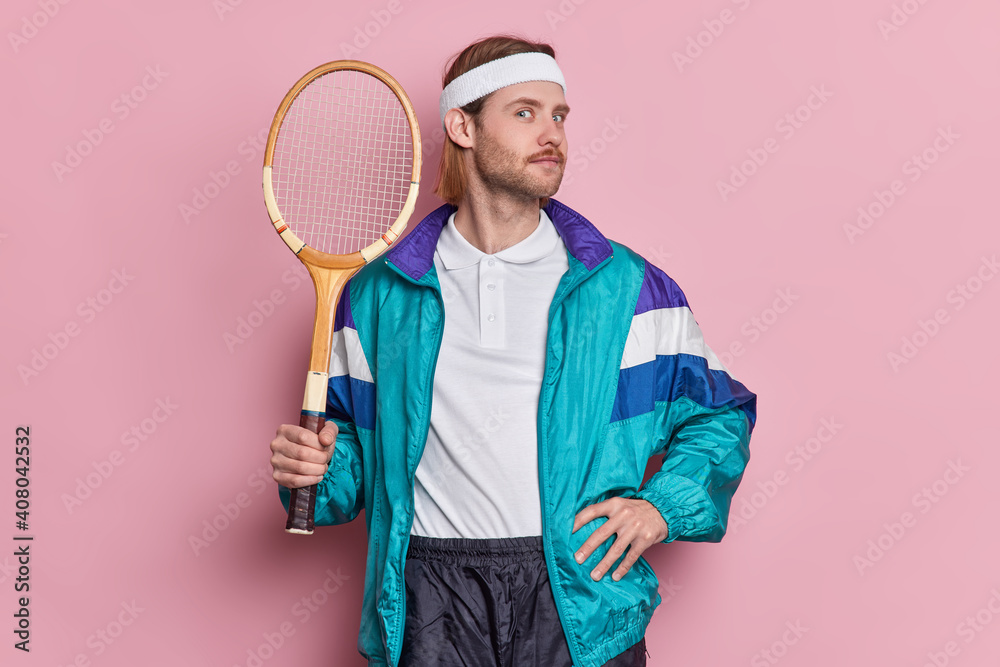 Active self confident sportsman holds tennis racket braggs about his winning of competition dressed in activewear enjoys game isolated over pink background. People and healthy lifestyle concept - obrazy, fototapety, plakaty 