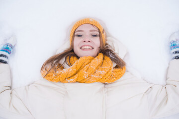 Wall Mural - Portrait of a happy smiling girl lying on the snow on a snowy winter day