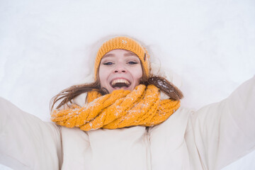 Wall Mural - Portrait of a happy smiling girl lying on the snow on a snowy winter day