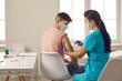 © Studio Romantic - Vaccination agaist coronavirus during epidemic concept. Young man patient in protective face mask sitting and getting injection to arm with syringe from young woman nurse in uniform in medical clinic