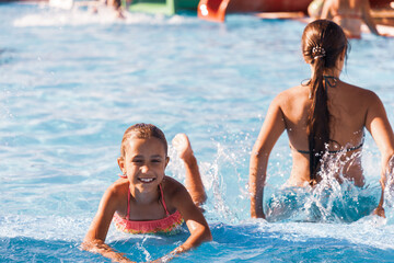 Wall Mural - Little cheerful girl playing in the pool with clear and clear water and looking smiling at the camera