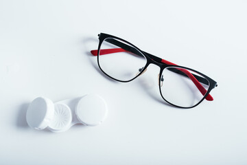 Top view of dioptric red-black glasses and white cover for contact lenses on a white background. Concept of medicare.