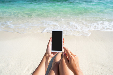 young woman using mobile phone at beautiful tropical white sand beach with wave foam and transparent