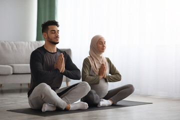 Wall Mural - Pregnant Muslim Woman In Hijab Meditating Together With Her Husband At Home