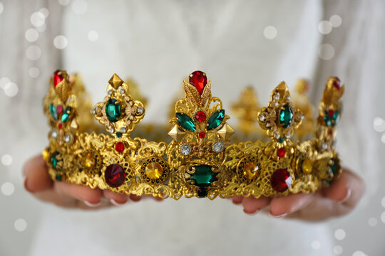 Woman holding beautiful crown with gems on light background, closeup. Fantasy medieval period