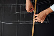 © DragonImages - Hands of tailor drawing bespoke jacket detail on black wool fabric, view from above