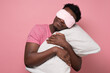 © Viktor Koldunov - African young man holding a white pillow, sleeping. Studio shot on pink wall.