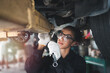 Female auto mechanic work in garage, car service technician woman check and repair customer car at automobile service center, inspecting car under body and suspension system, vehicle repair service sh