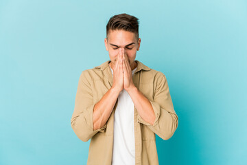 Young caucasian handsome man isolated holding hands in pray near mouth, feels confident.