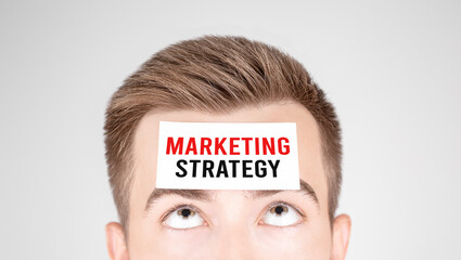 Poster - Man looking at paper with word Marketing Strategy, pasted on his forehead