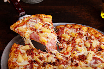 Hawaiian pizza with ham and pineapple cut into slices, cheese pull