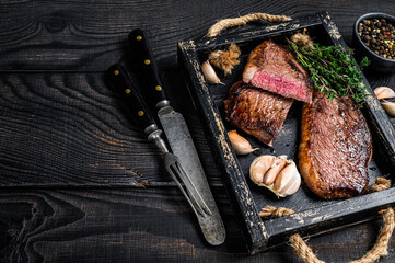 Wall Mural - Barbecue Grilled rump cap or brazilian picanha beef meat steak in a wooden tray. Black wooden background. Top view. Copy space