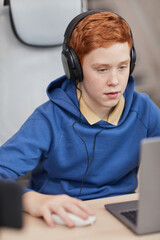 Wall Mural - Vertical portrait of red haired teenage boy playing video games at home with camera set up for online streaming