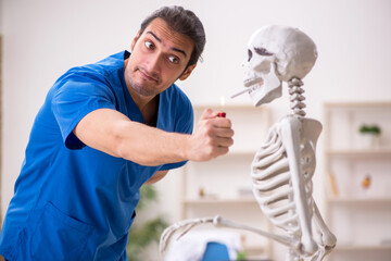 Wall Mural - Young male doctor and skeleton patient in antismoking concept