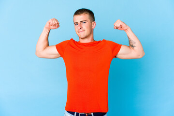 Young caucasian handsome man showing strength gesture with arms, symbol of feminine power