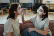 © pressmaster - Young female twins with facial clay mask sitting on couch in home environment