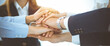 © rogerphoto - Business team showing unity with their hands together in sunny office. Group of people joining hands and representing concept of friendship, teamwork and partnership