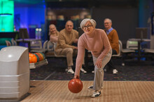 Full Length Portrait Of Joyful Senior Woman Playing Bowling With Group Of Friends In Background, Copy Space