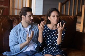 Fototapete - Unhappy young Caucasian couple have family misunderstanding or fight over smartphone usage or addiction. Angry man and woman family or lovers quarrel using talking on cellphone gadget at home.