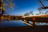 Fototapeta Pomosty - Illuminated bridge over a river in a city park at night