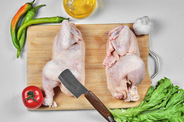 Raw half cut chicken with lettuce, peppers and tomato on wooden board