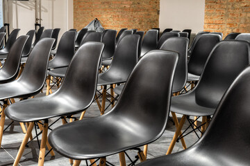 Rows of empty black chairs with red brick wall for grunge background. Selective focus. 