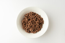 Chocolate Cereal Rings Falling In Bowl Isolated On White Background, Top View