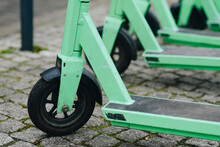 Close Up Of Wheel Of Green Modern Battery Operated Electric Scooters Parked In Row On Pavement, Waiting For Customers To Ride