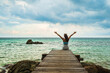 © geargodz - happy woman sitting on a wooden bridge with arm raised in the sea at Koh MunNork Island, Rayong, Thailand