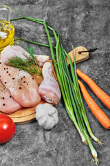 Raw chicken meat slices on wooden plate with fresh vegetables