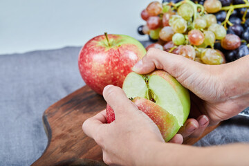 Cutting an apple into two halves and bunch of grapes on a wooden board