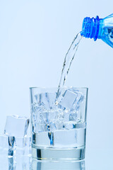 Wall Mural - Pouring clean drinking water from blue plastic bottle into glass on blue background