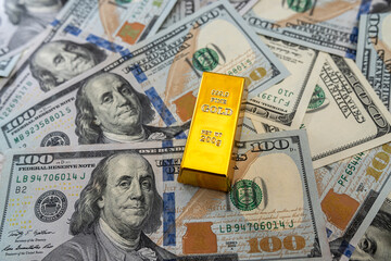 Gold bullion on pile us dollar bills as background