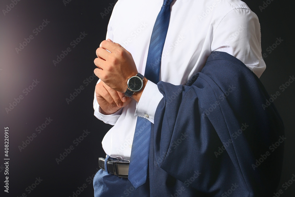 Young businessman with stylish wristwatch on dark background