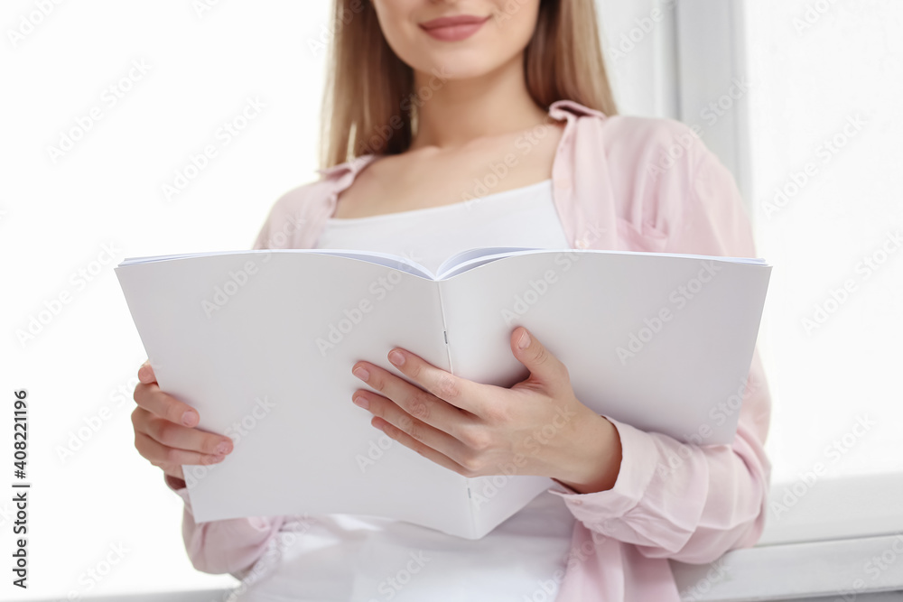 Beautiful woman reading blank magazine in room