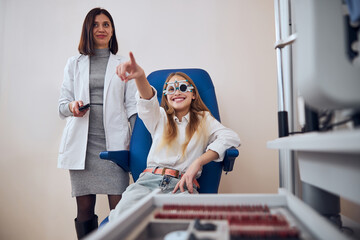 Wall Mural - Happy funny blonde lady showing to the something in front of her on optometrist cabinet