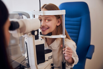 Wall Mural - Beautiful teenager girl talking with doctor optician while they examining her vision in ophthalmology center