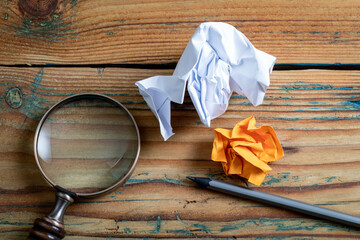 Wall Mural - Crumpled paper, pencil and magnifying glass on a wooden background. Education, information and data search concep