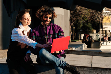 Two friends using a laptop together while sitting outdoors.