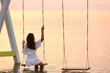 © New Africa - Young woman enjoying sunrise on swing over water