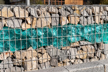 Close-up Detail Of New Modern Beautiful Gabion Fence With Metal Cage Filled By Crushed Stone And Shattered Artificial Blue Glass Rocks. City Street Road Pavement Protection