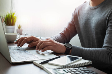 Close-up shot of man's hand with watch on his wrist. using keyboard of laptop computer on office desk. He is working business in office with copy space. Business investment-finance accounting concept.