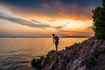 Sticker - Silhouette of a Young Man Fishing and Resting at a Tropical Beach during Sunset