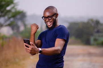 young african man standing outside and delighted while using his smart phone