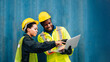 © BigBlues - worker team man and woman in protective safety jumpsuit uniform with yellow hardhat and use laptop check container at cargo shipping warehouse. transportation import,export logistic industrial service