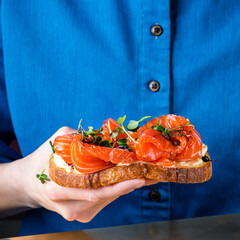 Wall Mural - Hand hold bruschetta with cheese and slices of red fish of fresh salmon, bruschetta with salmon in a woman's hand