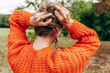 © iuricazac - A pretty young woman arrange her long red hair, making a hairstyle outdoors, wearing an orange sweater, posing on nature background.