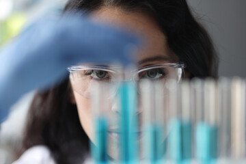 Portrait of woman in glasses who looks at test tubes with liquid